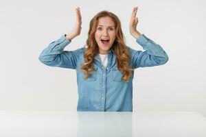 foto van jong agressief blond dame draagt in denim shirt, schreeuwen en looks boos met verheven handen, zittend Bij de wit tafel over- wit achtergrond.