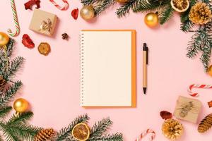 minimale creatieve platte lay van winterkerst traditionele compositie en nieuwjaarsvakantieseizoen. bovenaanzicht open mockup zwarte notebook voor tekst op roze achtergrond. bespotten en kopiëren van ruimtefotografie.