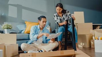 gelukkige Aziatische jonge aantrekkelijke paar man en vrouw helpen elkaar doos uitpakken en meubels monteren versieren huis bouwen tafel met kartonnen doos in de woonkamer. jong getrouwd aziatisch verhuisconcept. foto