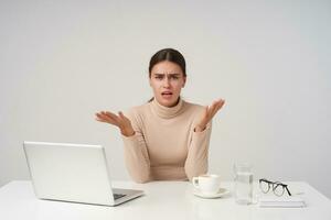 opgewonden jong mooi donker haren vrouw verhogen handen terwijl op zoek verward Bij camera, werken Bij kantoor met modern laptop, vervelend formeel kleren terwijl poseren over- wit achtergrond foto