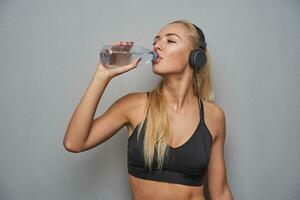 studio foto van jong blond lang haren vrouw met paardenstaart kapsel drinken water