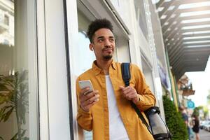 portret van jong ontevreden donker huid Mens, chatten Aan de telefoon met zijn vrienden, op zoek met haatdragend uitdrukking, zijn vriendin is laat opnieuw. foto