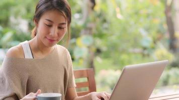 freelance aziatische vrouw die thuis werkt, zakelijke vrouw die op laptop werkt en koffie drinkt zittend op tafel in de tuin in de ochtend. levensstijl vrouwen die thuis werken concept. foto