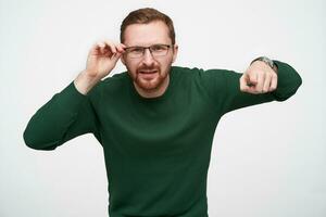 portret van verward jong gebaard Mens met kort kapsel Holding zijn eyewear terwijl op zoek verbaasd Bij camera, tonen verder met inhoudsopgave figer terwijl staand tegen wit achtergrond foto