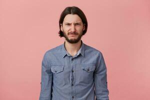 portret van gepijnigd jong gebaard Mens in denim shirt, looks verdrietig van streek beledigd hopeloos, opent mond net zo gaan naar schreeuw, geïsoleerd over- roze achtergrond. foto