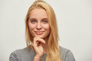 dichtbij omhoog van lief mooi blond jong vrouw met blauw ogen teder flirten lachend, hand- houdt kin, planning haar datum met vriend, geïsoleerd over- wit achtergrond foto