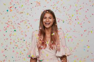 portret van gelukkig lief jong vrouw met lang geverfd pastel roze haar- draagt polka punt roze jurk lachend, vieren en hebben partij geïsoleerd over- wit achtergrond met confetti foto