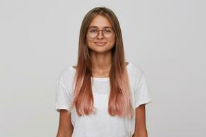 portret van glimlachen mooi jong vrouw leerling met lang geverfd pastel roze haar- draagt t overhemd en bril voelt gelukkig en zelfverzekerd geïsoleerd over- wit achtergrond looks direct in camera foto