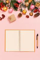 minimale creatieve platte lay van winterkerst traditionele compositie en nieuwjaarsvakantieseizoen. bovenaanzicht open mockup zwarte notebook voor tekst op roze achtergrond. bespotten en kopiëren van ruimtefotografie.