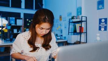 freelance azië vrouwen met behulp van laptop hard werken op nieuw normaal thuiskantoor. 's nachts thuiswerken, werken op afstand, zelfisolatie, sociale afstand, quarantaine voor preventie van het coronavirus.