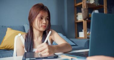 jonge Aziatische meisje tiener met casual gebruik computer laptop focus om online te leren schrijven lezing in digitale laptop in de woonkamer thuis. isoleer onderwijs online e-learning coronavirus pandemie concept.