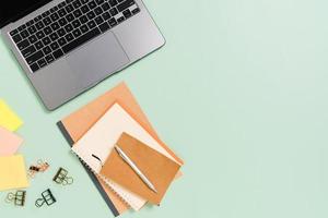 creatieve platliggende foto van een werkruimtebureau. bovenaanzicht bureau met laptop, koffiekopje en open mockup zwarte notebook op pastel groene kleur achtergrond. bovenaanzicht mock-up met kopieerruimtefotografie.