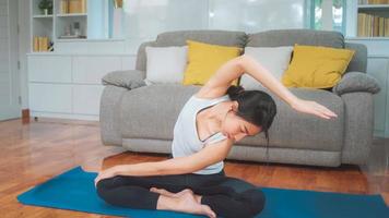 jonge aziatische vrouw die yoga beoefent in de woonkamer. aantrekkelijke mooie vrouw die thuis voor gezond uitwerkt. levensstijl vrouw oefening concept. foto