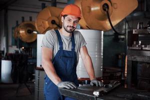 portret van een jonge arbeider met een helm in een grote metaalbewerkingsfabriek. de ingenieur bedient de machines en maakt onderdelen voor gasapparatuur