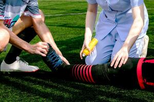 verpleegster is helpen een Amerikaans voetbal speler wie gewond zijn been terwijl spelen Amerikaans voetbal Aan de gras. foto