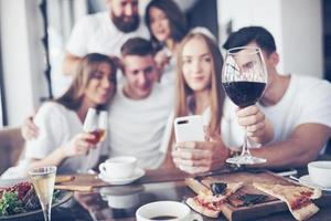 een groep mensen maakt een selfie-foto in een café. de beste vrienden verzamelden zich aan een eettafel, aten pizza en zongen verschillende drankjes