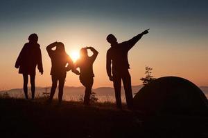 een silhouet van groepsmensen heeft plezier op de top van de berg bij de tent tijdens de zonsondergang