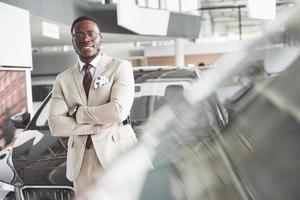 jonge zwarte zakenman op auto salon achtergrond. auto verkoop en verhuur concept foto