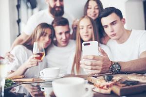 een groep mensen maakt een selfie-foto in een café. de beste vrienden verzamelden zich aan een eettafel, aten pizza en zongen verschillende drankjes