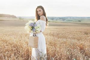 mooi meisje in witte jurk die bij zonsondergang op het herfstveld van tarwe loopt foto