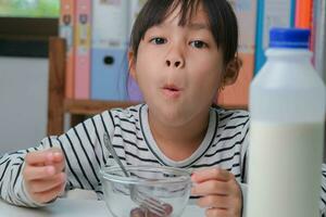 weinig meisje aan het eten vers rood druiven Bij huis in de leven kamer. schattig jong Aziatisch meisje eet gezond fruit en melk voor haar maaltijd. gezond voedsel in kinderjaren foto