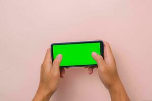 menselijk hand- gebruik makend van mobiel smartphone met mockup groen scherm Aan roze achtergrond. mannetje hand- spelen spel Aan blanco digitaal scherm. foto