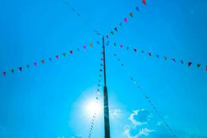 kleurrijk klein vlaggen in de lucht. golvend klein kleurrijk vlaggen hangende Aan de touw voor vakantie tegen blauw lucht. foto