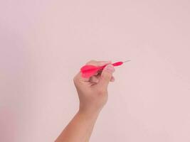 vrouw hand- Holding pijl geïsoleerd Aan roze achtergrond. detailopname hand- krijgen klaar naar Gooi een plastic pijl tip. foto