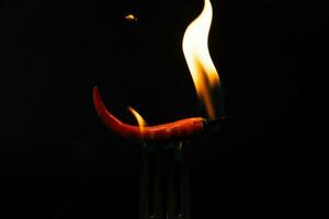 Chili peper Aan vork met vlammen Aan zwart achtergrond. brandend rood Chili peper. langzaam beweging foto