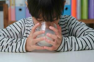 schattig Aziatisch meisje drinken een glas van melk Bij huis in leven kamer. weinig meisje drinken melk in de ochtend- voordat gaan naar school. gezond voedsel in jeugd. foto