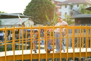 moeder en kinderen houding glimlachen en op zoek Bij de camera Aan de brug over- de rivier. khlong mae kha, een nieuw attractie in Chiang mei, Thailand. foto