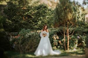 jong en mooi bruid met lang bruin haar- in een bruiloft jurk buitenshuis met een bruiloft boeket van bloemen. portret Aan de ts-e lens foto