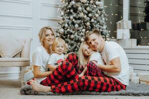 vrolijk en gelukkig familie met Kerstmis cadeaus in de buurt de Kerstmis boom in bij elkaar passen pyjama. kinderen zijn hebben plezier. liefhebbend familie met cadeaus in de kamer. foto