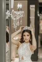portret van een meisje in een bruiloft jurk in de buurt een spiegel, met een kroon Aan haar hoofd. de concept van een Koninklijk feest. verticaal foto. foto