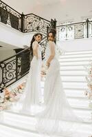 twee mooi meisjes in bruiloft jurken houding Aan de trap van een restaurant versierd met bloemen. foto schieten voor een bruiloft salon