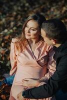 een Mens aangeraakt zijn zwanger vrouwen buik met zijn hand- terwijl resting in een herfst Woud Aan een vergeeld blad. ondersteuning van de man gedurende zwangerschap foto