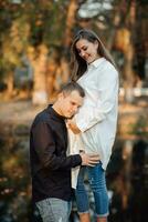 jong zwanger vrouw in een wit shirt. de man zetten zijn handen Aan zijn vrouwen maag en leunde tegen zijn oor. foto