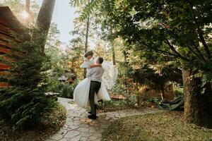 modieus bruidegom en schattig bruid in wit jurk met tiara van vers bloemen cirkelen en lachend in park, tuin, Woud buitenshuis. bruiloft fotografie, portret van glimlachen pasgetrouwden. foto