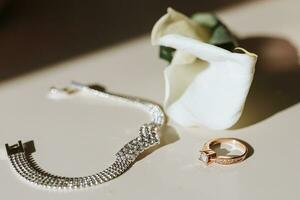 een corsages van calla bloemen en een goud bruiloft ring Aan de tafel en een zilver armband foto