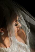 gelukkig en mooi bruid onder een sluier detailopname. bruid met professioneel bedenken en kapsel Aan een donker achtergrond. foto