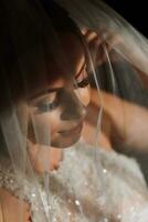 gelukkig en mooi bruid onder een sluier detailopname. bruid met professioneel bedenken en kapsel Aan een donker achtergrond. foto