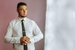 zakenman jurken en past zich aan zijn horloge, voorbereidingen treffen voor een ontmoeting. de bruidegom is voorbereidingen treffen voor de bruiloft. de Mens draagt een wit shirt. elegant bruidegom foto