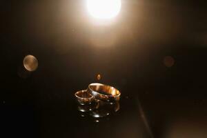 accessoires voor de bruidegom bruiloft dag. goud ringen Aan een donker achtergrond met achtergrondverlichting. Mannen mode foto
