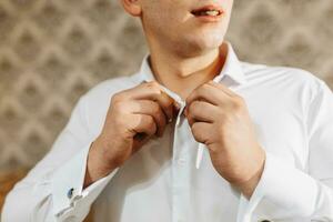 detailopname portret van een Mens Bij huis, knopen zijn shirt. de bruidegom is voorbereidingen treffen voor de bruiloft. de Mens is vervelend een wit shirt. elegant bruidegom foto