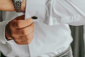 detailopname van Mens in wit overhemd aanpassen manchetknopen. de bruidegom zet manchetknopen foto