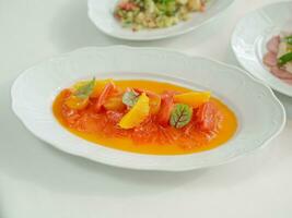 Zalm salade met oranje en basilicum in wit bord Aan wit tafel foto