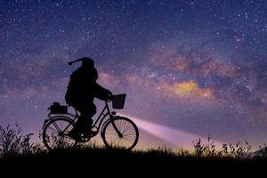 silhouet van de kerstman die op zijn fiets rijdt om een geschenk te dragen onder de melkwegachtergrond. foto