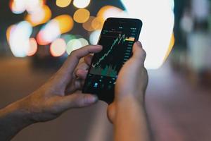 afbeelding van de hand van een man die zijn telefoon gebruikt om de beurs te controleren foto