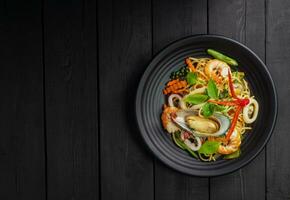zeevruchten dronken spaghetti met garnaal inktvis mosselen Chili, en basilicum. Thais voedsel. gezond Aziatisch in een bord Aan een zwart achtergrond tafel. top visie. foto