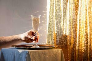 hand- Holding Champagne fluit in dienblad Aan tafel tegen goud sprankelend achtergrond foto